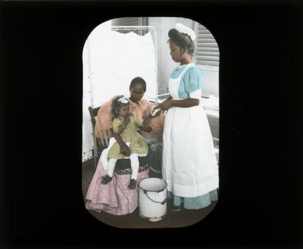 A nurse with a young girl and mother. The young girl is wearing gold bracelets commonly worn by children of more affluent families at the time, and her mother is wearing a "voluminous blouse of a sheer material" as Carrie Chapman Catt describes in her journal from the Philippines. The young girl is being held in her mother's lap while the nurse examines her hand.