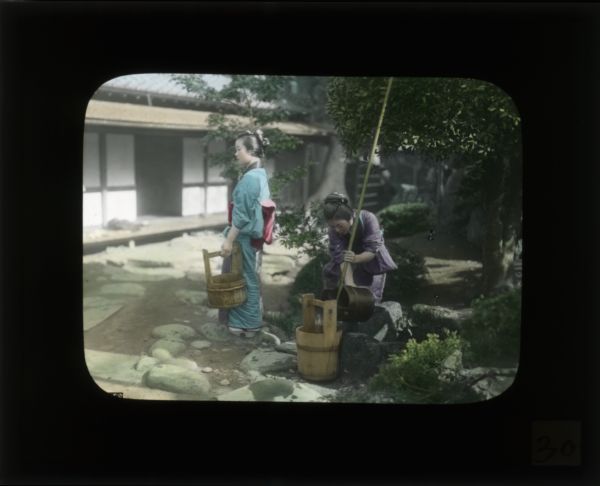 Two women filling wooden buckets in a courtyard. Both women are wearing kimonos.