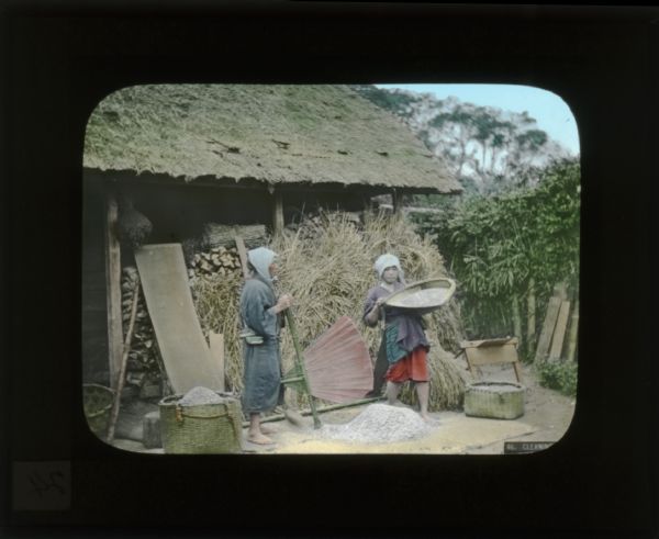 Two girls cleaning. One is carrying a basket while another holds a large fan-shaped object which was used like a broom. The description in the lower right of the image says "Cleaning".