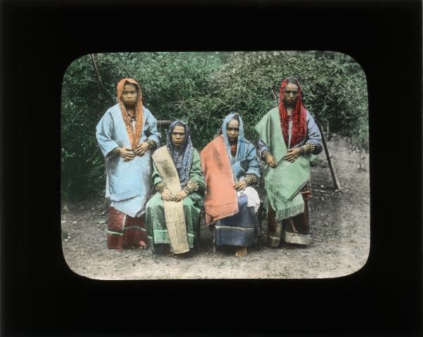 Group portrait of four women. Two women are seated and two are standing. They are all wearing shawls, skirts, and sashes. In her travel journals, Carrie often described the clothing of the local people.