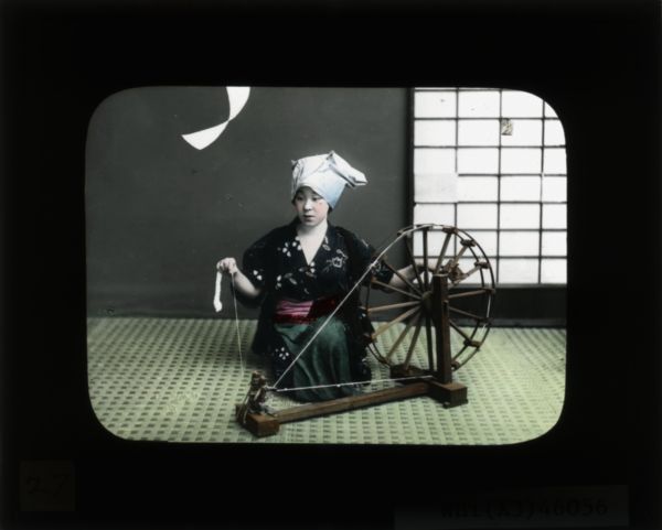 A girl using a type of spinning wheel. She is wearing a kimono and a head wrapping.