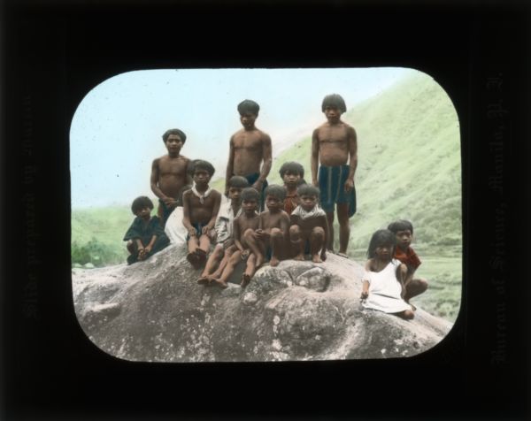 A group of children gathered on a rock. There is a mountain in the background. Carrie describes in multiple journals that children were rarely fully clothed. She also writes about what local children did for amusement day-to-day.