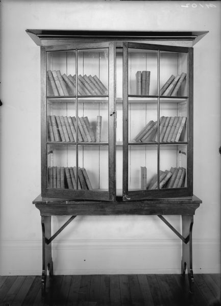 First bookcase at the Wisconsin Historical Society, with two glass paneled doors that are slightly open to show three shelves with books.