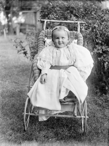 An outdoor portrait of Elizabeth Slaughter sitting in a wicker baby carriage.