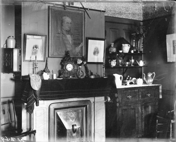 An interior view of the A.P. Morris residence. Portraits are above the mantel of the fireplace, on which sits an ornate clock and other objects. To the right is a buffet with serving dishes.