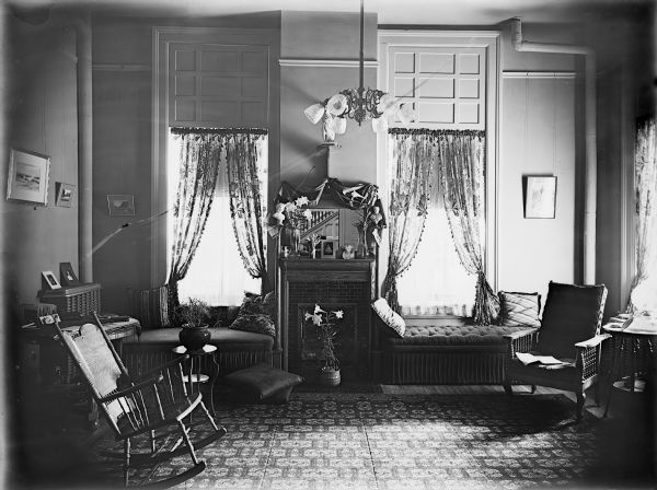 Miss Mayhew's room in the Ladies' Hall, located on the University of Wisconsin campus. The room is set for Easter, with Easter lilies on the mantel and on the floor in front of the fireplace. There are window seats in front of the windows flanking the fireplace.