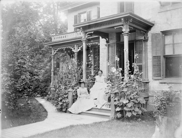 Three women are sitting on the porch steps of Professor Allen's home, located on Langdon Street. Two of the women hold hand fans in their lap.