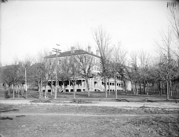 A southeast view of the University of Wisconsin-Madison Ladies' Hall. In the foreground two men are working in the road among piles of dirt and rock.