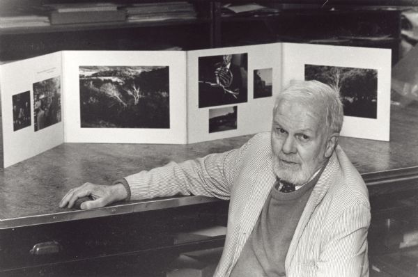 Paul Vanderbilt, the curator emeritus of Iconographic collections at the State Historical Society of Wisconsin, poses in front of one of his Thematic Panels that is positioned on a table. He created 96 "thematic panels" that combine historical photographs, his own photographs and lines of his own poetry.