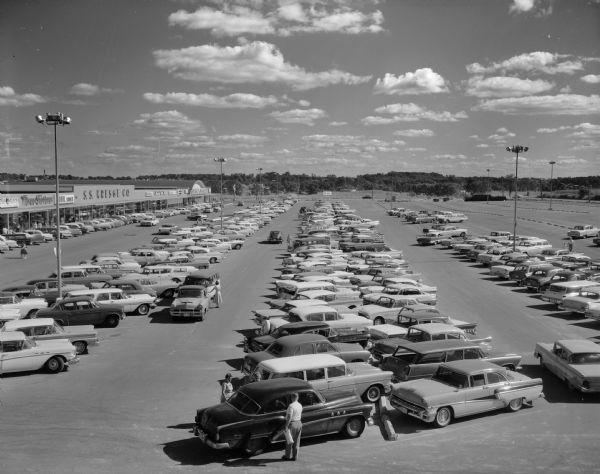 Elevated view of the parking lot at the Westgate Shopping Center. The storefronts are on the left, and include Ragatz Shoes, Three Sisters, ?obil Shoes, S.S. Kresge Co., Pearson and the Piggly Wiggly.