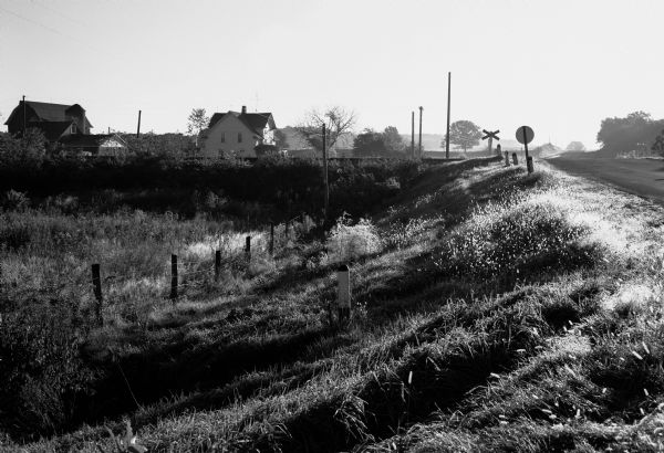 Early morning at a railroad crossing on County Highway A, with houses and a barn in the distance.