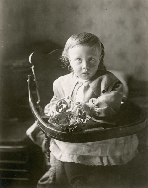Young child seated in a highchair. An ornate basket sits on the tray.