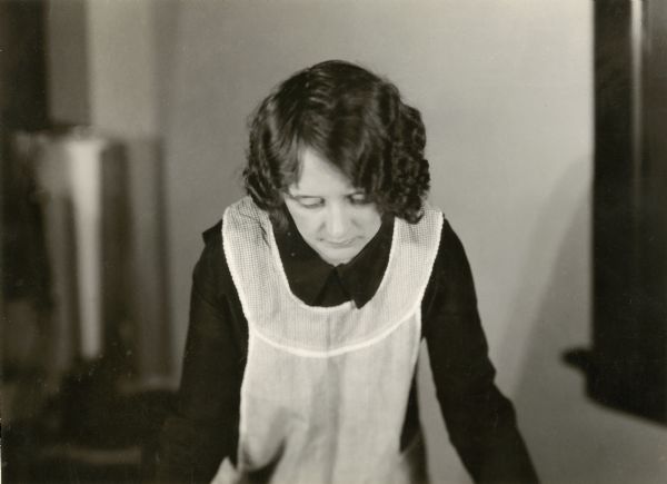 Young housewife wearing apron, leaning forward and looking down. Photograph for the extension project of the International Harvester Co. of Chicago.
