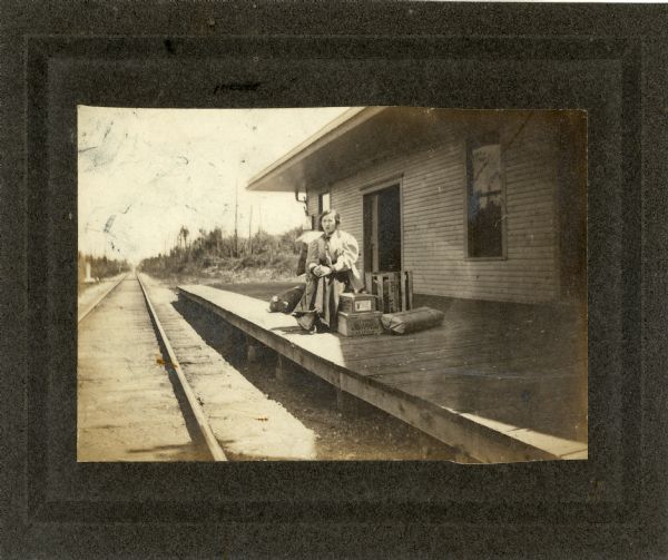 Woman seated among parcels on the train platform of an isolated small railroad station.