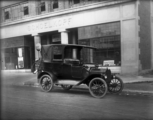 View from street towards a 1914 or 1915 Ford Model T parked at the curb in front of the Schoelkopf dealership at 210 E. Washington Avenue.