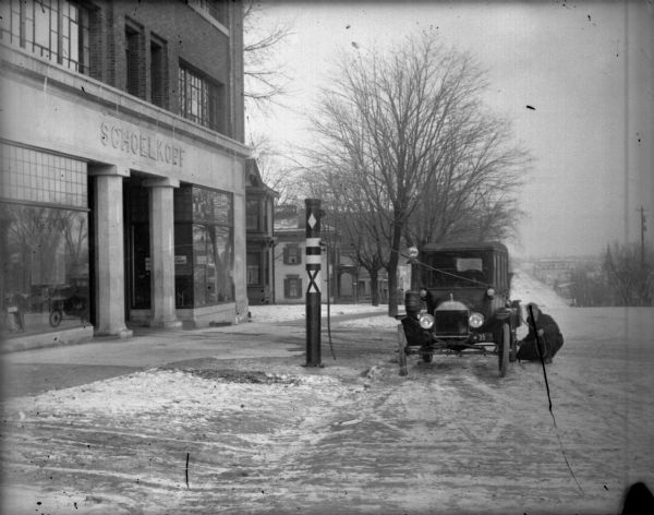 View along curb towards a man crouching in the street to add air to a tire from the pump in front of the Schoelkopf Ford dealership at 212 E. Washington Avenue in the winter.