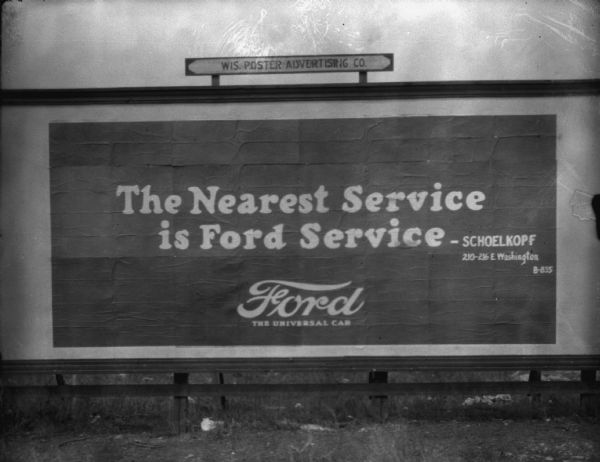 Outdoor view of a billboard from the Wis. Poster Advertising Co. promoting the Schoelkopf Ford dealership with an ad: "The Nearest Service Is Ford Service — Schoelkopf 210-216 E. Washington B-835. Ford, The Universal Car."
