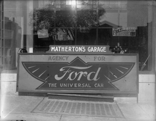 Sign on sidewalk for Matherton's garage, an agency for "Ford, The Universal Car." Location unknown. The sign is set up in front of a show window, which has a sign for "Use Frazzle Soap." There were many Ford service and dealerships in Wisconsin in the 1920s.