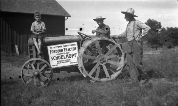 Two men and a boy in front of a barn are posed with a Fordson tractor. The two men are wearing straw hats. A sign on the tractor reads: "We Are Power Farmers Using Fordson Tractor Purchased from Schoelkopf, Authorized Ford Sales and Service, Madison Wisconsin."

Fordson tractors were manufactured by the Henry Ford Company from 1916 through the 1930s all over the world, but only sold from 1918-1928 in the United States.