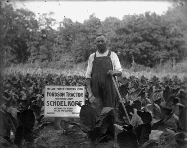A middle-aged man stands holding an agricultural implement in a field of tobacco plants. A sign next to him reads: "We Are Power Farmers Using Fordson Tractor Purchased from Schoelkopf, Authorized Ford Sales and Service, Madison, Wisconsin."

Fordson tractors were manufactured by the Henry Ford Company from 1916 through the 1930s all over the world, but only sold from 1918-1928 in the United States.