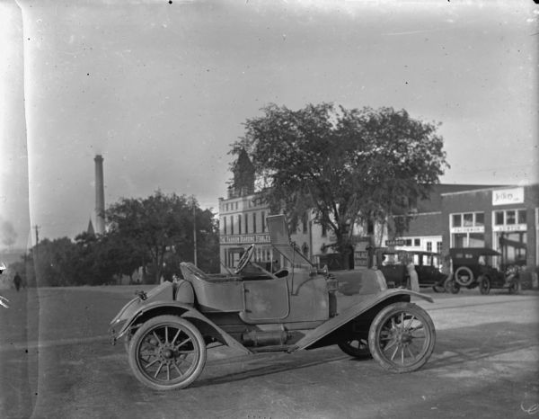 Right side view of a Ford Model T Runabout parked in the middle of East Washington Avenue. On the right side of the street in the background is the Fashion Boarding Stables, which is next door to the Palace Livery and a garage. In the far background is a smokestack.