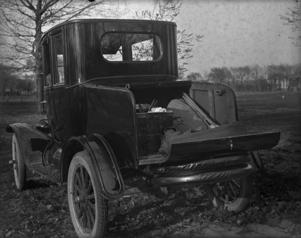 A pickup truck or an automobile with the trunk open, sits in a field.