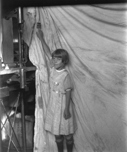 A young girl is standing  in front of a curtain while reaching up a hand to push a button that will open Air-Lec automatic doors. Equipment is on the left.