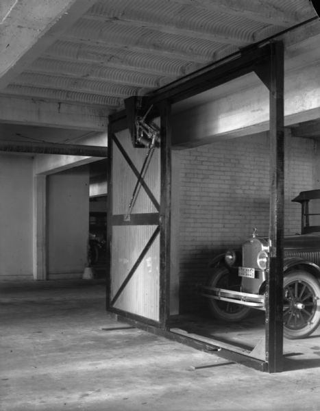 Indoor view of an Air-Lec automatic door opener on a sliding garage door. There is a Ford car in the garage stall. The license plate on the car is 30-033.