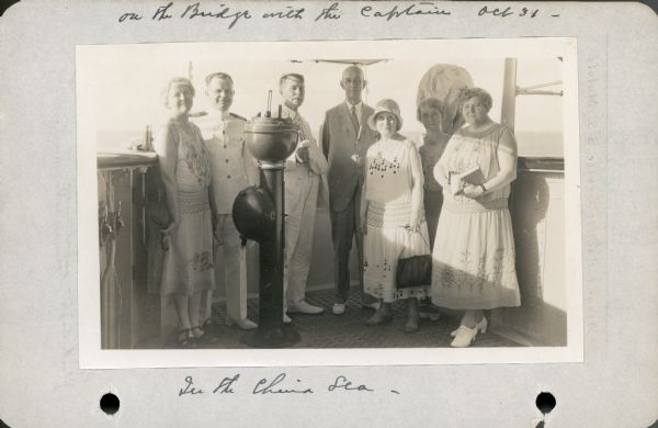 Alma Seipp Hay, second from right, and her  husband, William Sherman Hay, third from left, join Commander C.W. Berndtson and other passengers on the bridge of the <i>S.S. Malolo</i>. The binnacle compass stands in front of the commander. This photograph is from Mrs. Hay's journal which documented their three month Pacific cruise.