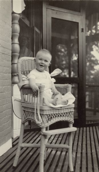 Young Edward Petersen (1921-2013) poses sitting in a wicker highchair on the porch at Black Point. He is the son of William F. and Alma Schmidt Petersen and the great-grandson of Chicago brewer Conrad Seipp. His grandmother, Emma Seipp Schmidt, observes from the screened porch behind him.