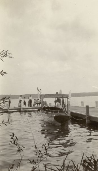 View from shoreline of Dr. Otto Schmidt, second from left, standing on the pier at Black Point with other, unidentified, adults and children. A launch is tied at the pier and there are three sailboats in the distance. Dr. Schmidt was married to Emma Sybilla Seipp, the daughter of Chicago brewer Conrad Seipp, who built his summer home at Black Point.