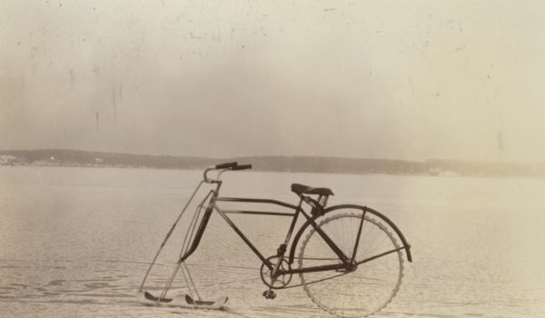 A bicycle which has been modified for travel on ice stands on frozen Geneva Lake. The front wheel of the bicycle has been replaced by a ski; the rear wheel has a studded surface.