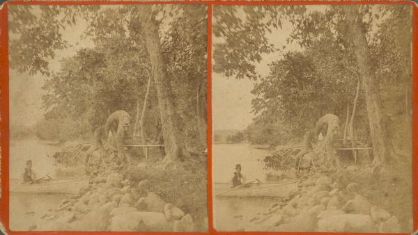 Stereograph view along shoreline of Geneva Lake at Porter's Park. A man sits in a canoe at the rocky shoreline while a woman sits and reads on a rustic bench between two trees.