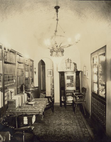 A room off the entrance hall of the Edward Petersen home at 1322 Astor Street in Chicago's Gold Coast area has a barrel vaulted ceiling and bookcases along the left wall. A "mineral cabinet" is built into the right wall above a radiator. There is an oriental carpet on the floor and a  large chandelier.