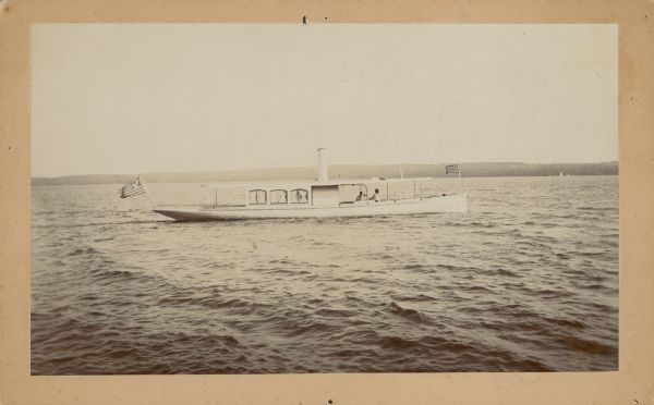 View across water towards the steam launch "Cygnet" with enclosed cabin and smokestack. The "Cygnet" belonged to H.A. Beidler, who developed Cedar Point near Williams Bay on Geneva Lake.