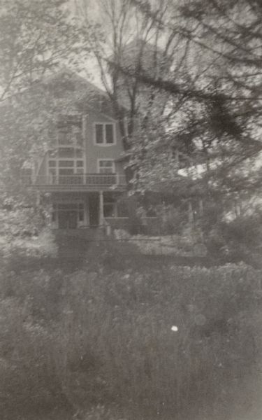 View looking up hill, from near the shore of Geneva Lake, towards the main house at Black Point. Doors facing the lake on the first and second floors open onto porches. The distinctive tower is partially obscured by foliage.