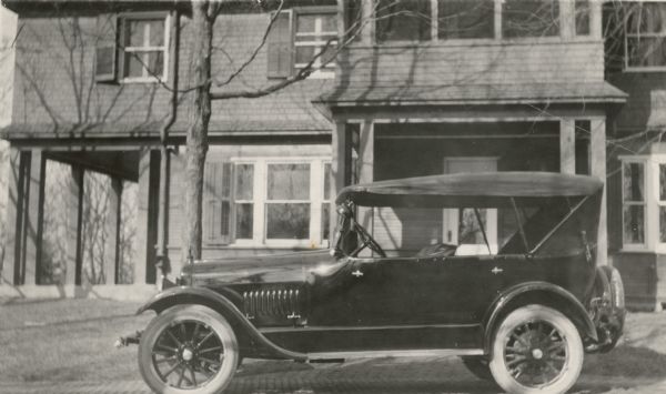 A Studebaker automobile is parked on the brick drive in front of the 1905 cottage at Black Point Estate. The side and front porches on the first floor are open. There is a screened porch above the front porch, and there are shutters on the windows.