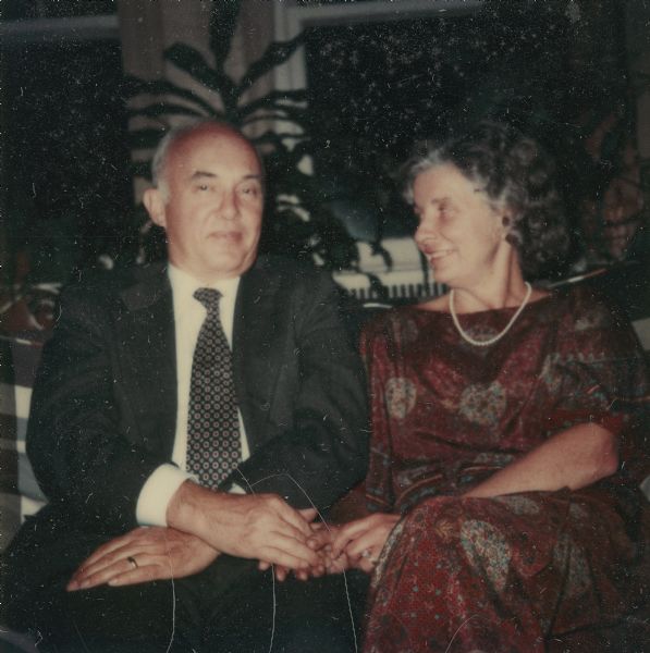 William Otto Petersen and his wife Jane Jordan Browne Petersen pose seated and holding hands for a portrait around the time of their wedding. He is wearing a suit and tie; his wife is wearing a long dress and a string of pearls.