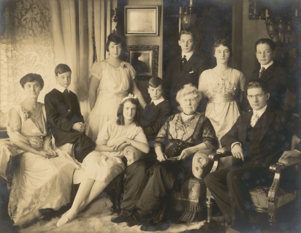 Catherine Orb Seipp, widow of prominent Chicago brewer and founder of Black Point Estate, Conrad Seipp, poses in her Chicago home with her nine grandchildren.  They are, seated, from left, Alma Schmidt, Otto Madlener, Elsa Bartholomay, William Madlener (Otto's twin brother), Mrs. Seipp, and Ernst Schmidt.  Standing, from left, are Catherine Bartholomay, Henry Bartholomay, Clara (Tessa) Schmidt, and Albert F. Madlener, Jr.  All are wearing dress clothing.  On the reverse of the photograph is written, "Photograph taken in drawing room of 1300 Michigan Ave.  Pale blue satin draperies, cream colored lace curtains.  Gold and blue chairs.  Polar bear rug."