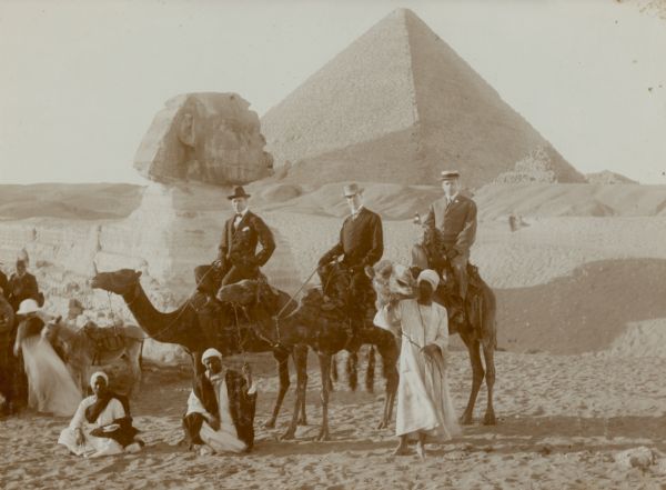 Three men in western dress riding camels pose with their Egyptian guides in front of the Sphinx at the Giza necropolis, with the Cheops pyramid in the background.  Identified on the photograph's mat are Conrad Seipp Jr., center, and Donald Dallas, far right.  Seipp, the youngest child of Chicago brewer Conrad Seipp, died January 19,1909 in Cairo, not long after this photograph was taken.  He was on a pleasure trip through southern Europe and Egypt.