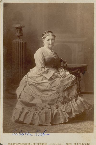 A seated, full-length studio portrait in front of a painted backdrop of Sibylla Orb. She is wearing a long dress with a full skirt trimmed in lace and ruffles. Her daughter, Cathrine Orb, was the second wife of Chicago brewer Conrad Seipp, who established Black Point Estate.