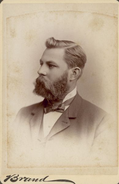 Vignetted three-quarter head and shoulders studio portrait of Christoph Hotz (1841-1904). He has a full beard and is wearing a suit coat, vest and necktie.