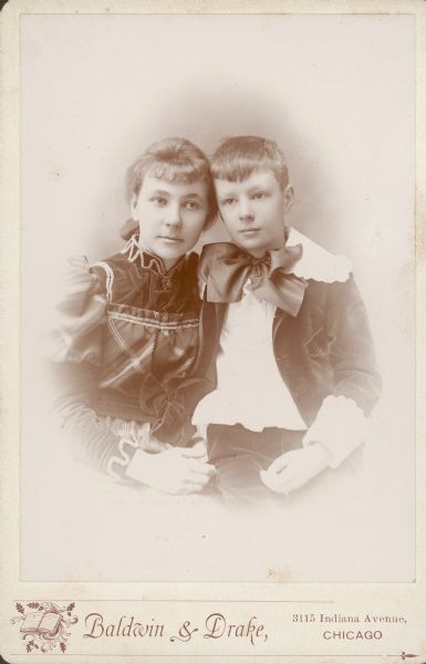 Waist-up vignetted studio portrait of brother and sister. Conrad Seipp (1883-1909) sits on the lap of his sister Alma (1876-1966) for a half length studio portrait. He is wearing a suit and white shirt that has a large lace collar and cuffs; he also sports a large bow tie. Alma's dress has metallic trim. They are the youngest children of Chicago brewer Conrad Seipp, who built Black Point Estate.
