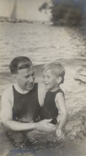 William F. Petersen holds his son Conrad in the waters of Geneva Lake off the shore of Black Point. There are sailboats in the background.