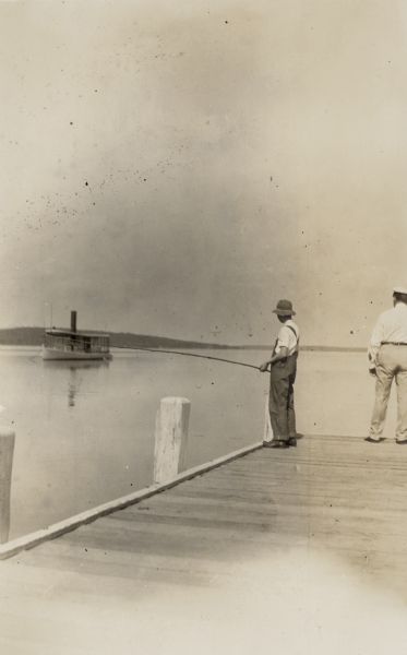 Henry Bartholomay Jr., right, and his son Henry Conrad Bartholomay fish on the pier at Black Point. The steamer <i>Loreley</i> is anchored offshore on he left.