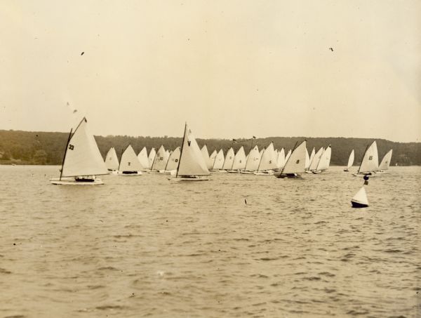 The start of the Class "C" race of the Inland Lake Yachting Association Regatta at Lake Geneva. Ernst Schmidt wrote in a description of this photograph, "59 boats started in one of the races. This buoy [right, foreground] was placed near the Lake Geneva Country club."