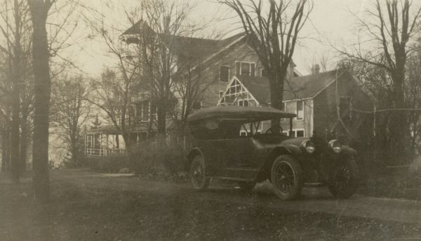 A Locomobile brand car is parked on the drive at Black Point near the "laundry," the rear section of the house that served as temporary living quarters for the family while the main portion of the house was being built. It later served as laundry and kitchen for the main house, and as living quarters for the staff. The porch and tower of the main house are in the background behind trees.