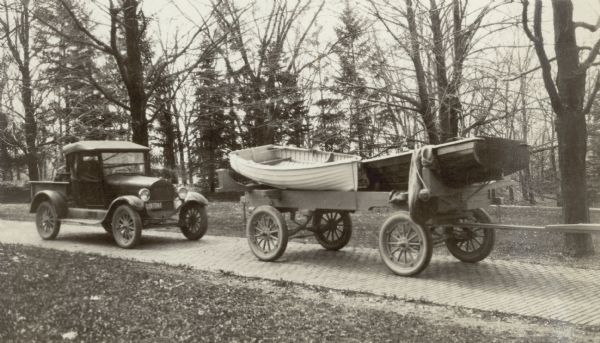 A trailer loaded with two new dinghies is parked on the brick drive at Black Point Estate. An automobile identified as "Thompson's Ford" is parked behind it. The dinghies had been recently built by John Nelson of Lake Geneva.
