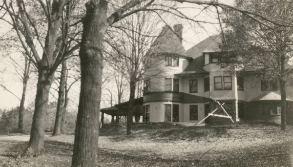 A side view of the Lake Geneva summer home of Albert and Elsa Seipp Madlener shows progress during remodeling. A portion of the porch has been removed and there is a temporary support in place.
The building is a two and one-half story wood sided Queen Anne style house with a corner tower and large side bay.