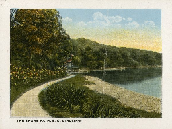 Halftone print of the landscaped shoreline and path at Forest Glen, the estate of Edward G. Uihlein, on the western end of Geneva Lake. A flag flies above a boathouse in the background, and there are several piers along the shore.
